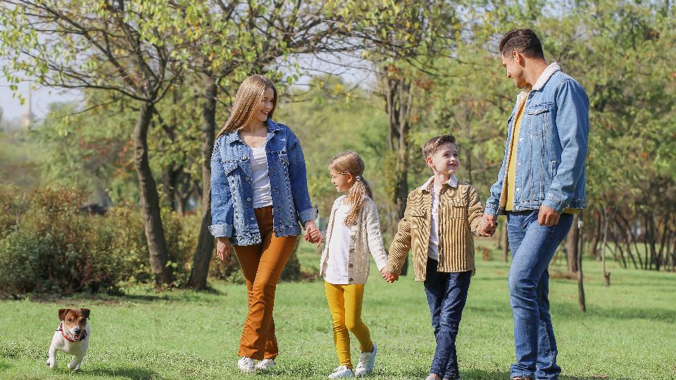Una familia camina por una plaza: mamá, papá, una nena, un nene y su perro.