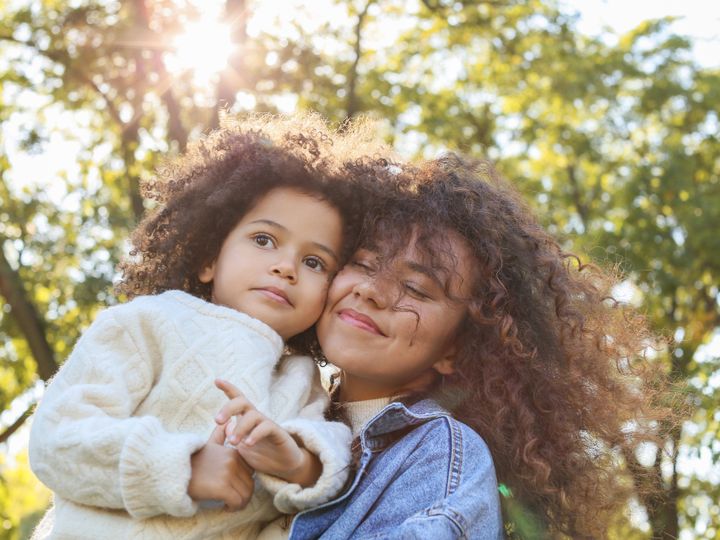 Una mamá abraza a su hija al aire libre.
